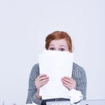 Frightened and insecure woman is hiding behind papers